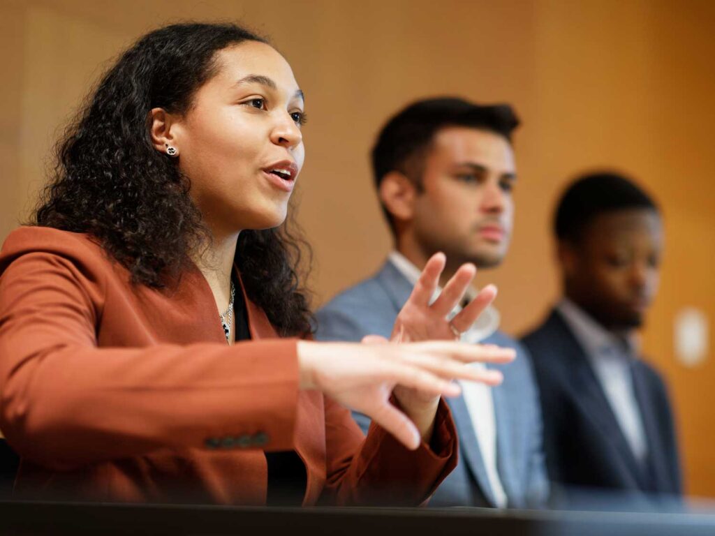 A Dyson student in the foreground speaks passionately with her hands while two other Dyson students listen in the background.
