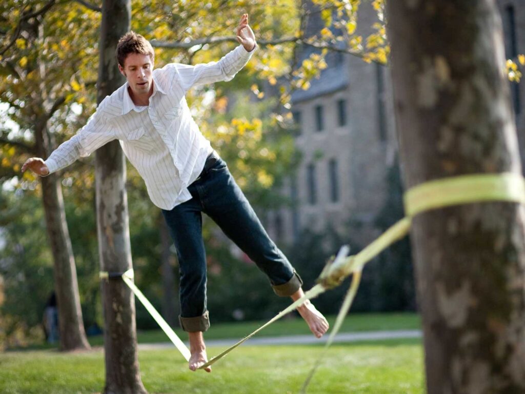A student on a slack line that’s between two tree outside of Warren hall.