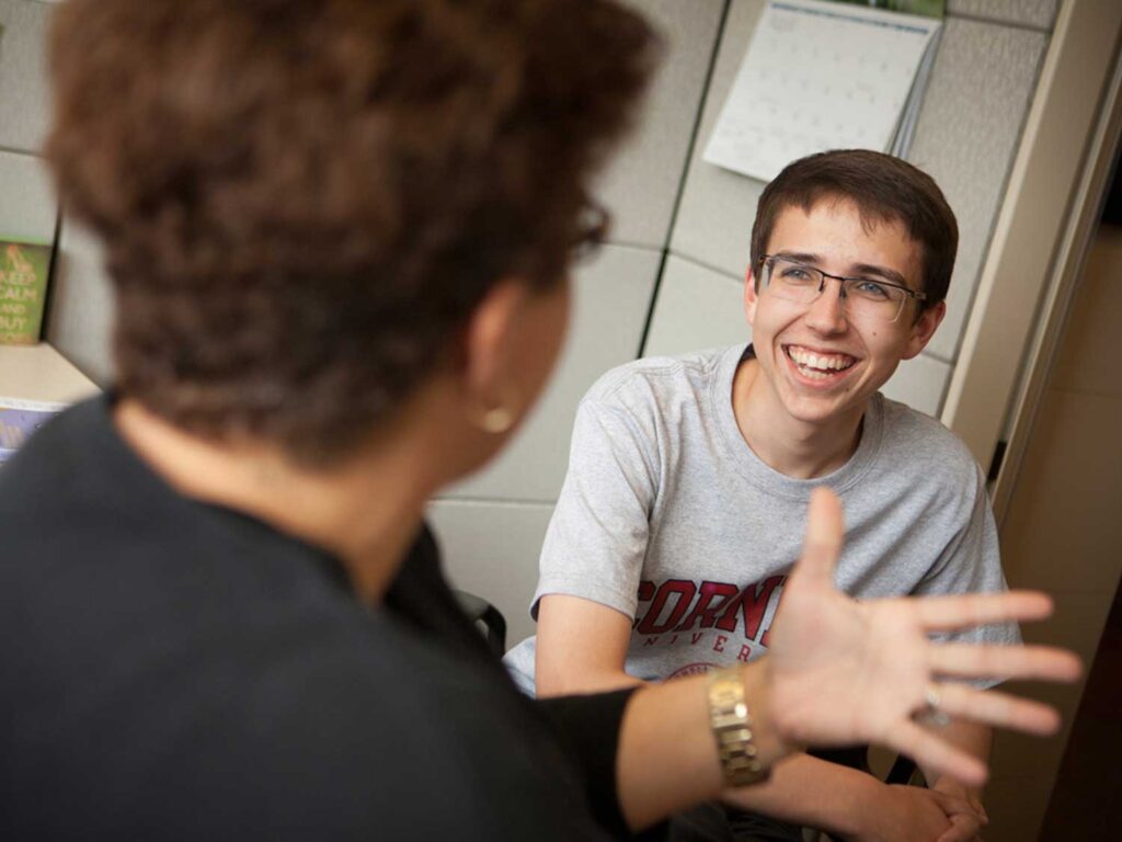 A student in a Cornell t-shirt smiles broadly at a professor.