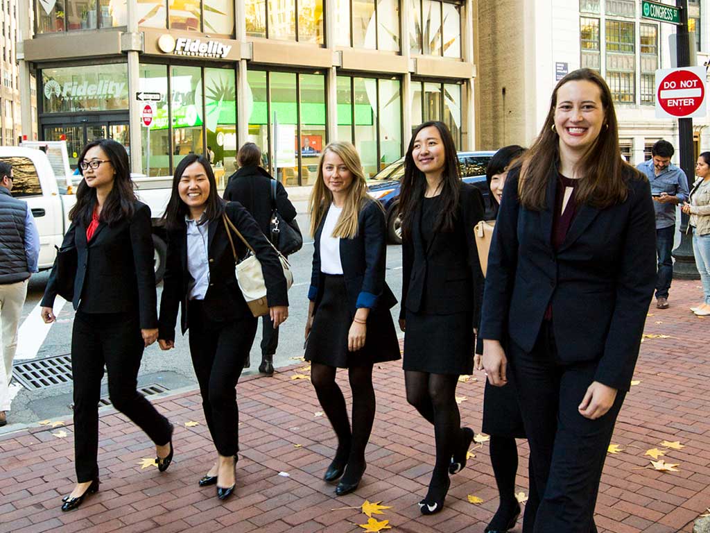 Students dressed in business attire walk on the sidewalk.