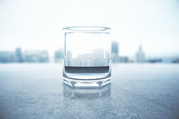 Glass of water with city reflection on concrete surface.