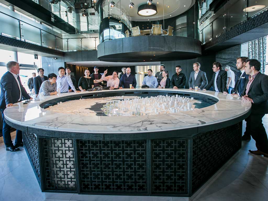 People standing and talking around a large circular replica of a cityscape.