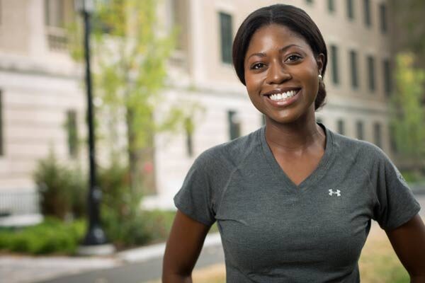 Woman in a v-neck t-shirt smiling in front of Warren Hall.