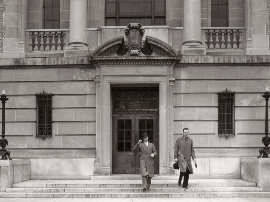 Historic black and white image of two men walking down the stairs of Warren Hall.