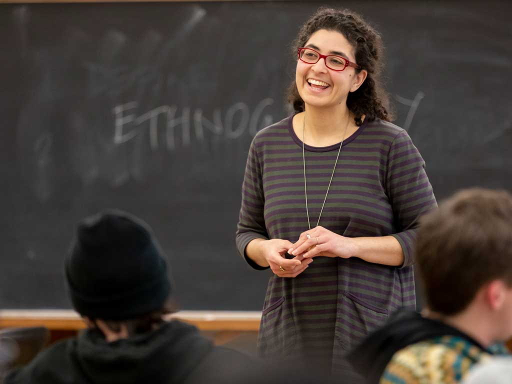 Headshot of Senior Lecturer Denise Ramzy stands in front of a chalkboard