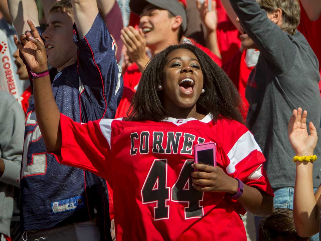 Woman wearing a Cornell jersey cheering at a Cornell sporting event.