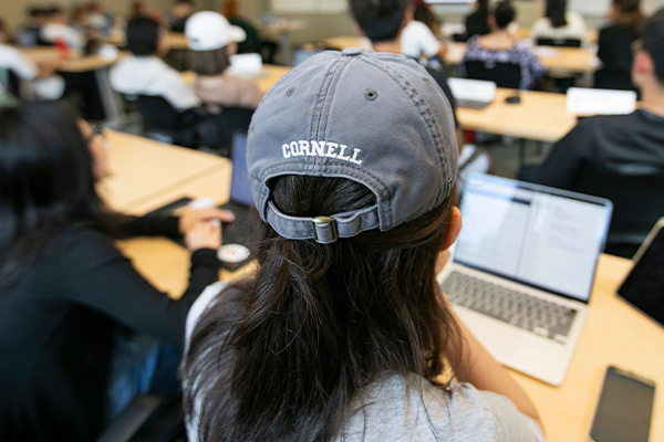 A student in class with her back turned wearing a hat with the word Cornell.