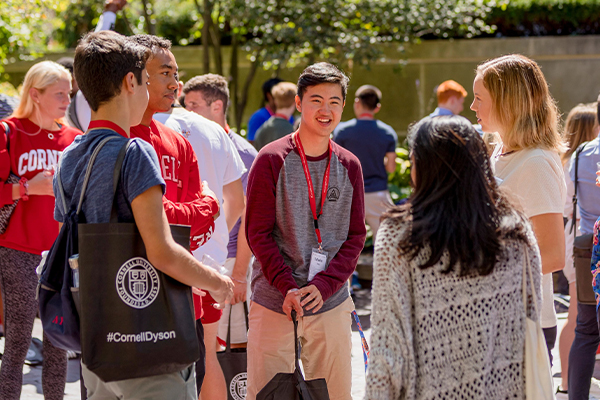 Students standing in a circle outside holding "#CornellDyson" tote bags.