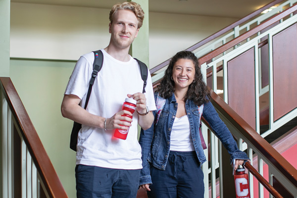 Two students standing at the bottom of the stairs with backpacks.