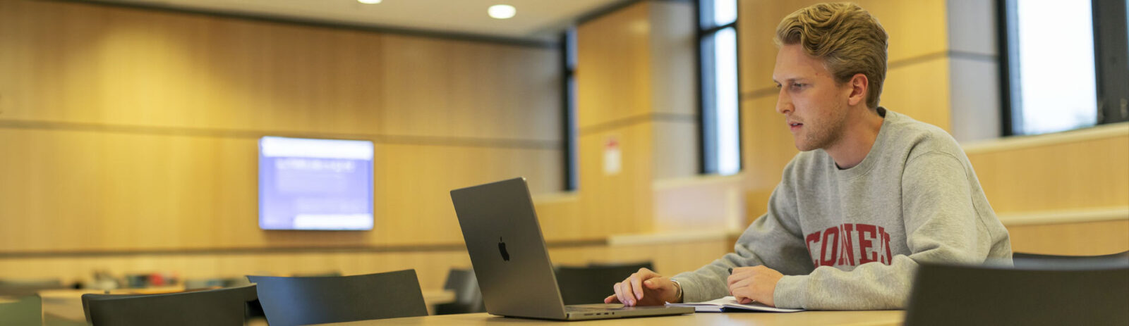 Student in a Cornell sweatshirt sits in front of a laptop at a table.