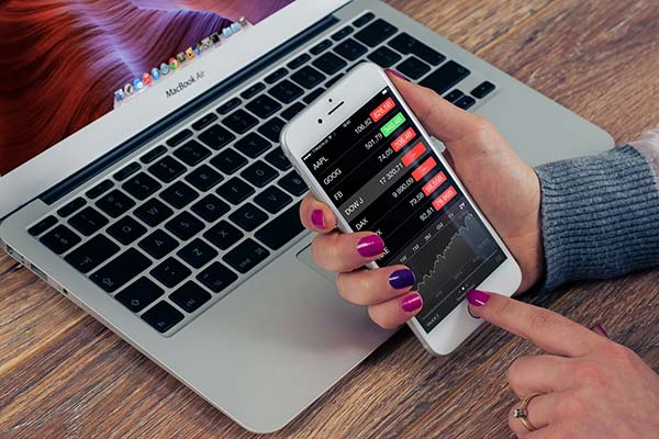 Image of a woman's hand using a phone in front of a computer with financial rankings.