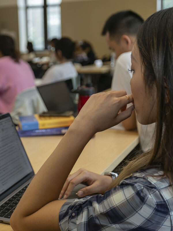 A student sits at a desk looking at a laptop screen in a classroom.