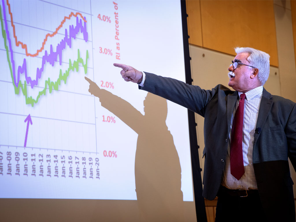 Man in suit points at a chart on a projector screen.