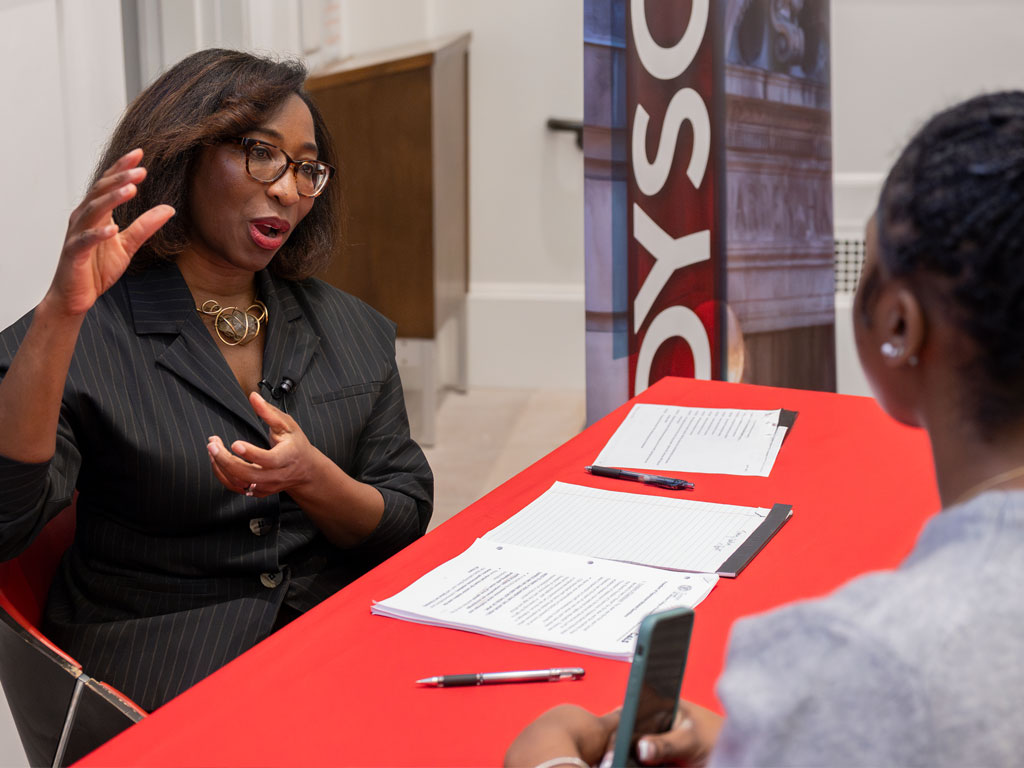 Woman in a pinstripe suit talks with her hands to another person.