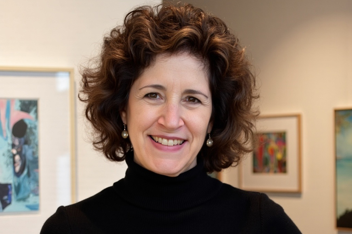 Headshot of a woman with brown curly hair standing in an art gallery.