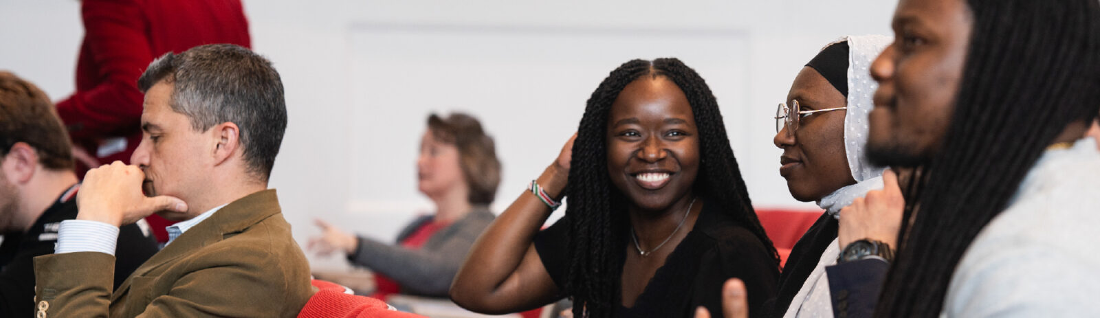 A person smiling sitting next to more people in a lecture hall.