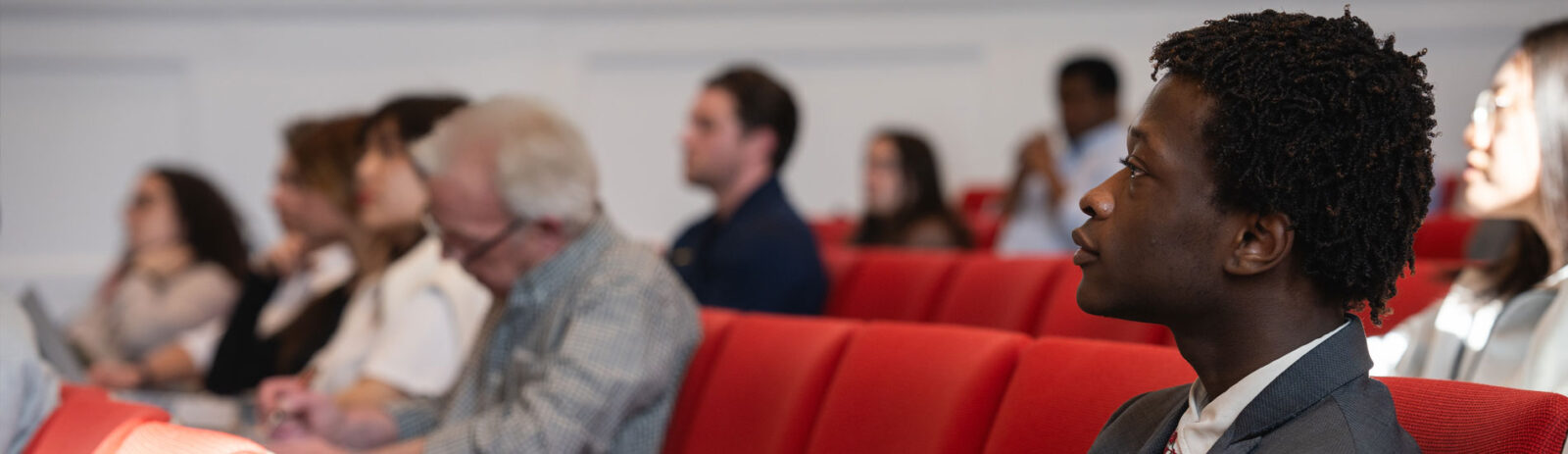 A person smiling sitting next to more people in a lecture hall.